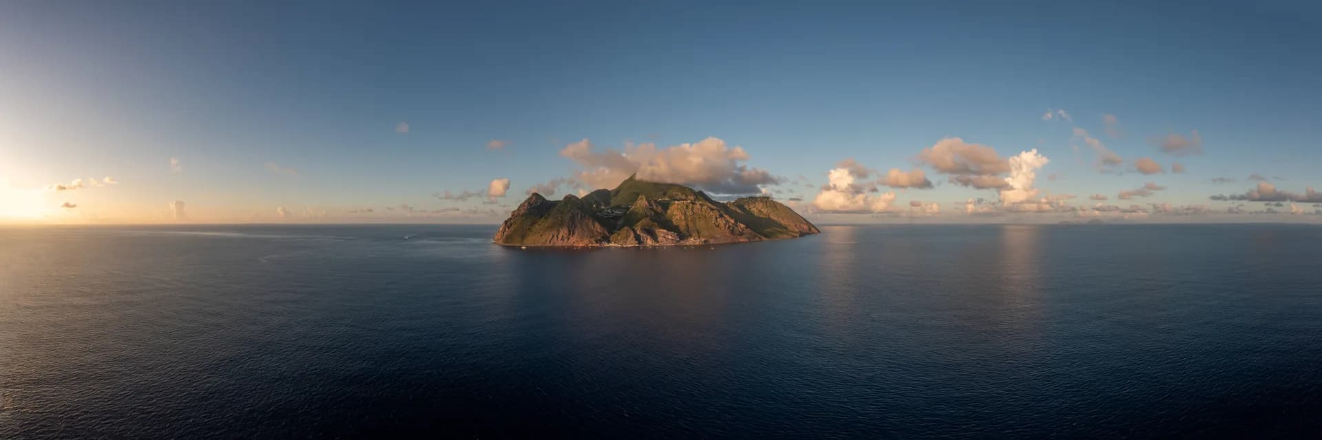 Aerial view of Saba rising from the Caribbean Sea at golden hour, surrounded by deep blue water.